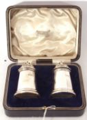 Cased heavy pair of George V peppers of castle type with pierced domed lids and urn finials, 8cm