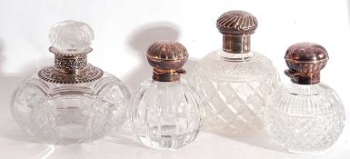 Group of four cut glass table scent bottles to include a Victorian large bottle with silver neck and