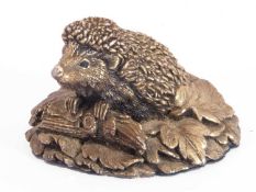 Modern silver hedgehog paperweight, seated in a bed of leaves, the front legs resting on a log,