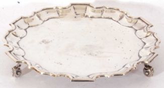 George V card salver, having raised Chippendale style border supported on three scrolling feet, 18cm