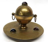 Brass inkwell on circular stand with ring handles, the stand with three glass or garnet balls