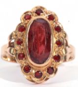 Mid-grade yellow metal dress ring centring a lozenge shaped red stone in rub-over setting, the