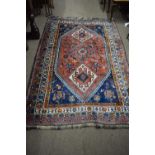 Middle Eastern wool floor rug decorated with large central red lozenge surrounded by a geometric