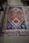 Middle Eastern wool floor rug decorated with large central red lozenge surrounded by a geometric