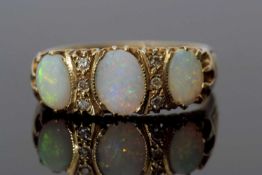 Three stone opal and diamond ring featuring three graduated oval shaped opals, highlighted between