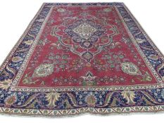 Large Iranian wool floor rug decorated with large central motif on a red background, surrounded by a