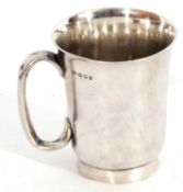 George V silver mug of flaring cylindrical form, plain polished design, C-scroll handle on a plain