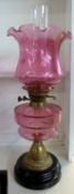 Oil lamp with cranberry tinted frilled shade over a cranberry font and brass base, total height