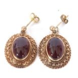 Pair of yellow metal and garnet set earrings, the oval cut cabochon centres in cut down settings and