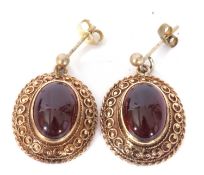 Pair of yellow metal and garnet set earrings, the oval cut cabochon centres in cut down settings and