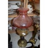 OIL LAMP WITH UNUSUAL GRENADE FORMED BASE, BRASS FONT AND A CRANBERRY TINTED SHADE