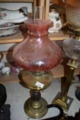 OIL LAMP WITH UNUSUAL GRENADE FORMED BASE, BRASS FONT AND A CRANBERRY TINTED SHADE