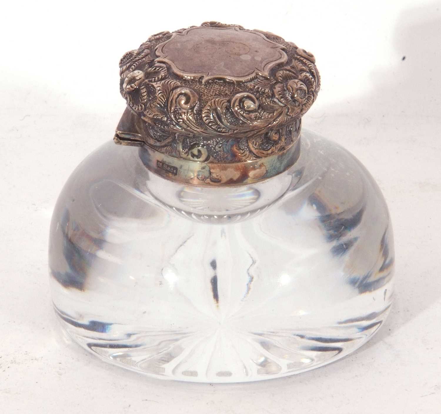 Circular clear glass inkwell with star cut base, hinged silver lid with embossed floral and