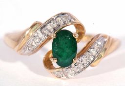 Modern 9ct gold emerald and diamond cross over ring, the oval faceted emerald set between diamond