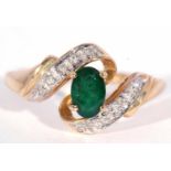 Modern 9ct gold emerald and diamond cross over ring, the oval faceted emerald set between diamond