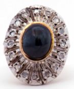 Large dress ring centring a dark oval cabochon bezel set sapphire, raised above a diamond set plaque