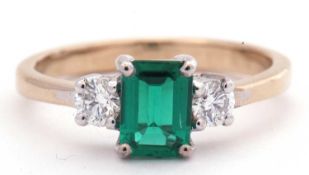 Emerald and diamond three stone ring, the step cut emerald flanked by two round brilliant cut