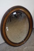 LATE 19TH CENTURY OVAL BEVELLED WALL MIRROR IN DARK WOOD FRAME WITH CARVED DECORATION, 87CM HIGH
