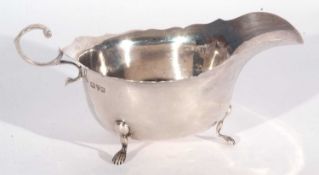 George V oval sauce boat of typical form with card cut rim, flying scrolled handle and supported