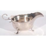 George V oval sauce boat of typical form with card cut rim, flying scrolled handle and supported