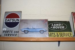 Three small thin metal advertising signs 'Datsun Parts and Service', 'Jaguar E-type' and 'Land