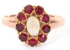 Opal and garnet cluster ring centring an oval cabochon opal raised within a small garnet surround (