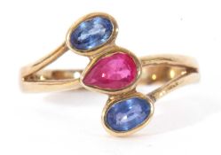 Sapphire and ruby three stone ring, a stylised design centring a pear shaped ruby between two oval