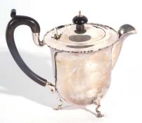 George V silver teapot of circular form having a hinged lid with an ebonised urn finial and scroll