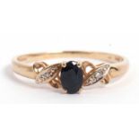 Modern 9ct gold dark sapphire and diamond ring, the oval shape faceted sapphire raised between small