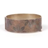 A silver hallmarked hinged bracelet, the top section chased and engraved with a floral design,