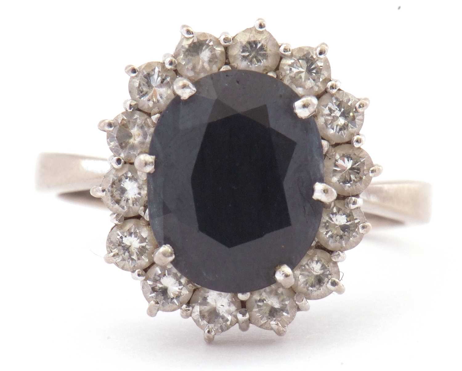 18ct white gold, dark sapphire and diamond ring, the oval faceted sapphire is 10x8mm, raised above a