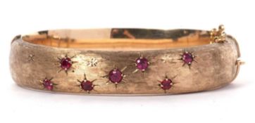 9ct gold and ruby set hinged bracelet, the top section a burnished design set with seven round cut