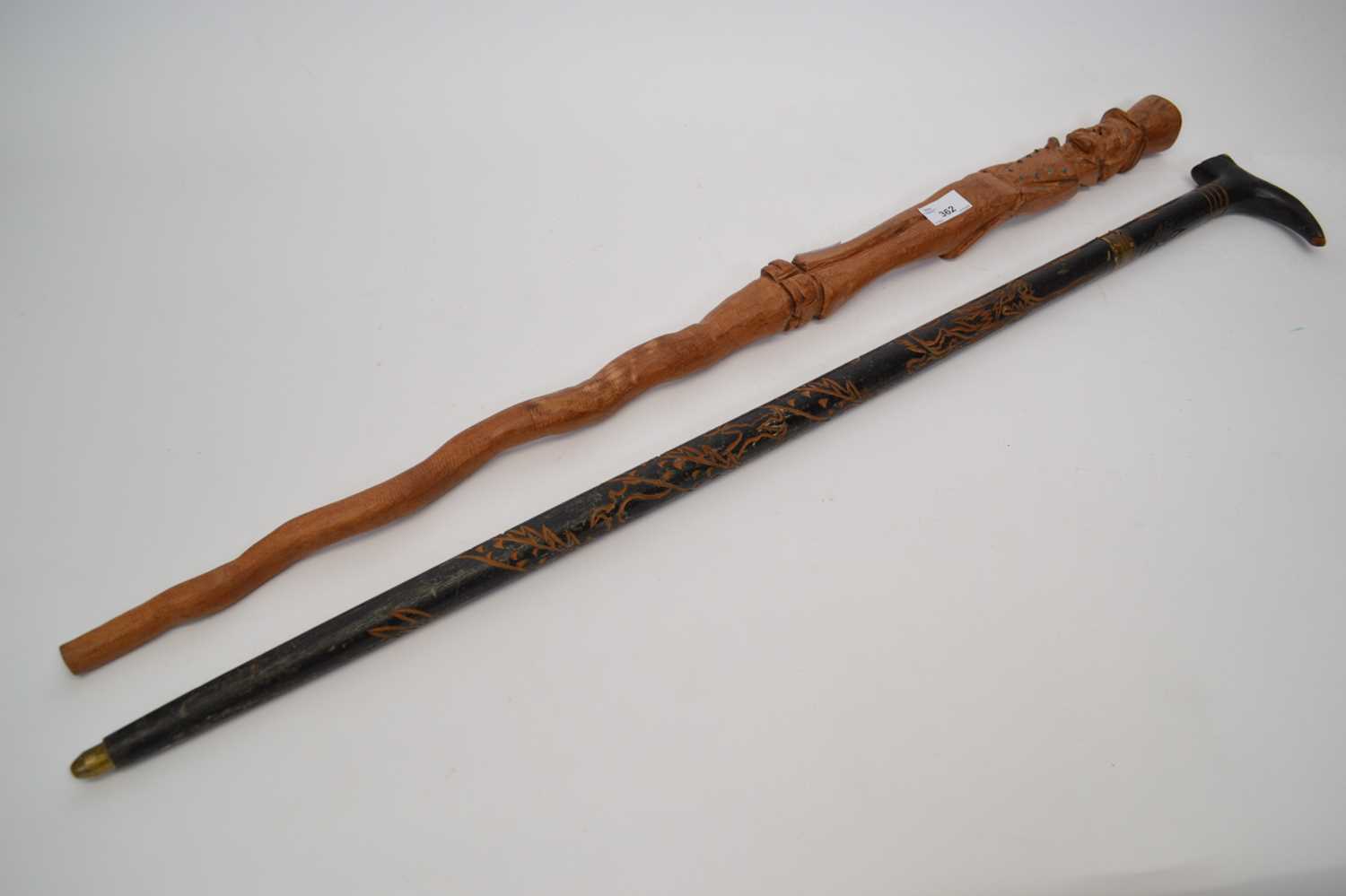 Ebonised wooden sword stick with a carved design together with a further walking stick with a carved