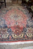 20TH CENTURY WOOL FLOOR RUG DECORATED WITH LARGE CENTRAL PANEL MAINLY IN RED AND BLUE, 275 X 182 CM