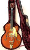 An electric guitar marked 'Gretsch (by Bigsby) Chet Atkins' in burnt orange, marked with serial
