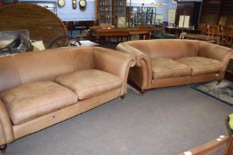 A pair of modern brown leather two seater sofas raised on turned legs with brass castors