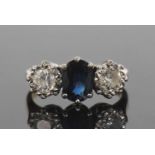 Sapphire and diamond three stone ring centering a dark oval shaped faceted sapphire flanked by two