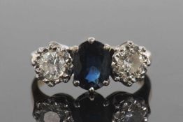 Sapphire and diamond three stone ring centering a dark oval shaped faceted sapphire flanked by two