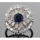 A circular sapphire and diamond cluster ring centering a round faceted sapphire raised above a