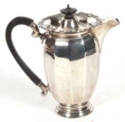 George V silver hot water jug of panelled form, the hinged lid with ebonised urn finial, the rim