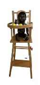 A vintage plastic baby doll with gold hoop earrings in wooden high-chair.