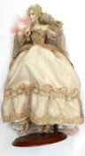 A porcelain doll on stand, formed as a lady in masquerade ball gown, with feathered face mask and