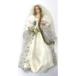 A porcelain doll on stand, formed as a bride, in white gown with lace veil and golden details.