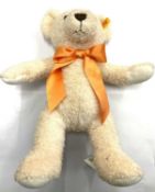 A 2015 Steiff teddy bear: 38 Creme Cosy Year. With orange bow and gold Steiff rivet and label to