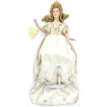 A porcelain doll on stand, formed as a lady in cream gown with floral detail, with plastic and