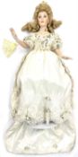 A porcelain doll on stand, formed as a lady in cream gown with floral detail, with plastic and