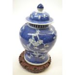 Chinese porcelain ginger jar and cover on carved wooden stand with prunus decoration on a blue