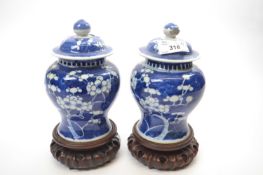 Two small Chinese porcelain jars and covers and wooden stands, the blue ground with prunus