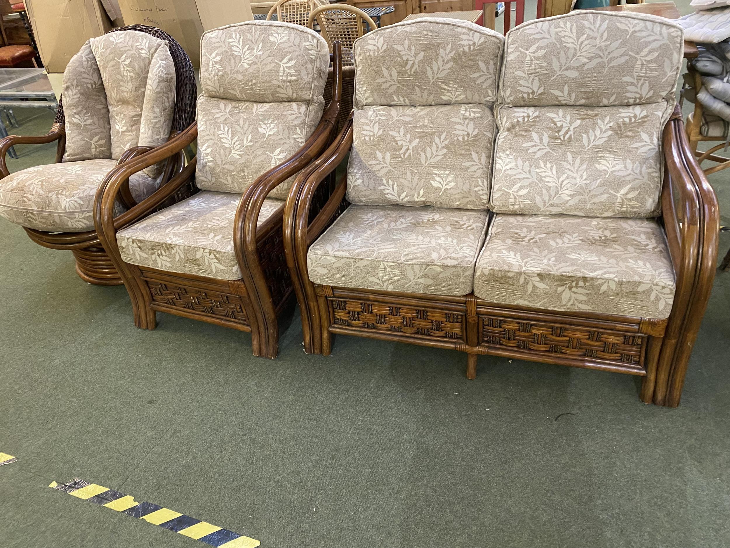 A dark brown cane sofa and chair suite, with loose cushions, tilting and revolving arm chair