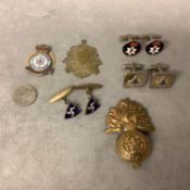 A collection of yellow and white metal cufflinks, a watch fob and two military metal insignia